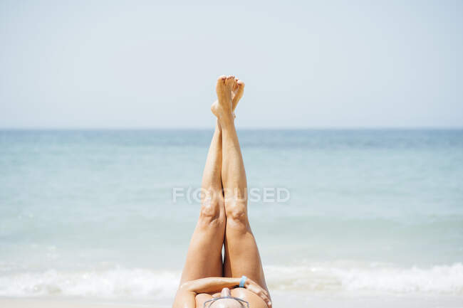 Mujer con los pies arriba acostada en la playa durante el día soleado - foto de stock