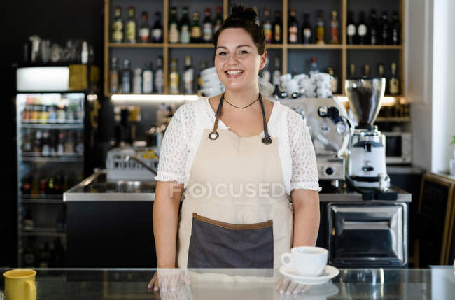 Dueña sonriente con café en el mostrador de la barra de pie en la cafetería  — servicio, Veinte años - Stock Photo | #479910300