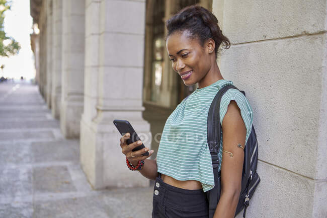 Smiling woman using phone while standing against column in city — Stock Photo