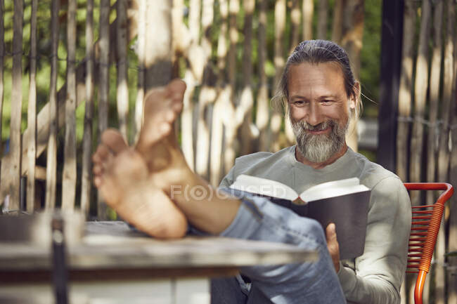 Smiling bearded man reading book while relaxing on chair in yard — Stock Photo