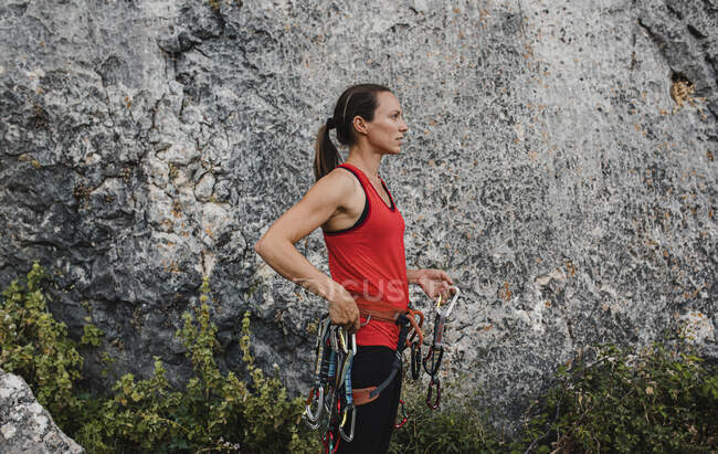 Fiduciosa arrampicatrice con imbracatura di sicurezza e moschettoni in piedi accanto alla roccia — Foto stock