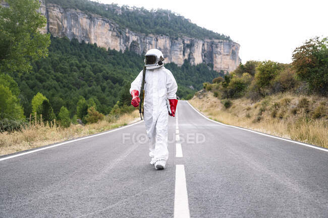 Astronauta masculino vestindo terno espacial andando na estrada contra a montanha — Fotografia de Stock