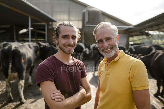 Retrato de granjero maduro feliz con hijo adulto en casa de vaca en una granja - foto de stock