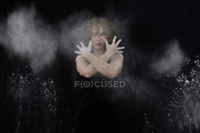 Woman throwing white dust besides herself while standing against black background - foto de stock