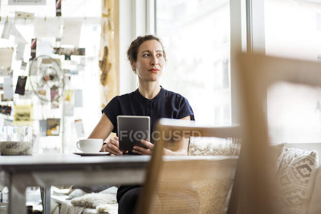 Задумчивая владелица с кофе на столе с помощью цифрового планшета в ресторане — стоковое фото