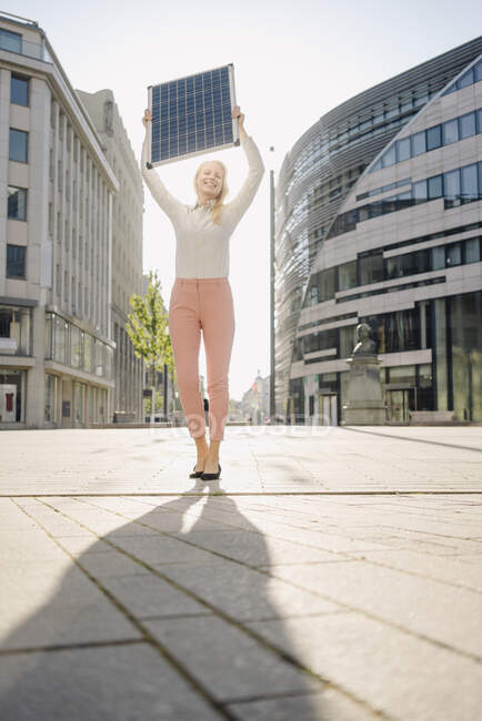Felice donna d'affari tenendo pannello solare mentre in piedi sul sentiero nel distretto finanziario — Foto stock