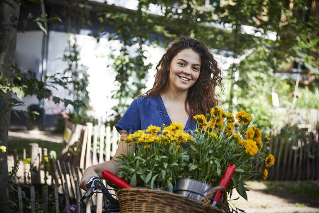Молода жінка з квітковими горщиками в кошику велосипеда. — стокове фото