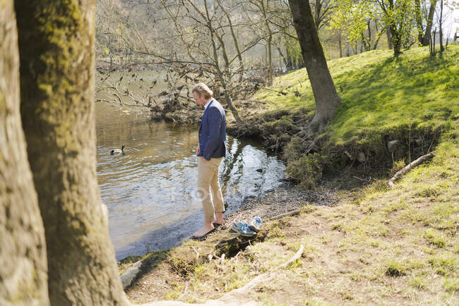 Imprenditore maschio in piedi alla riva del fiume nel parco nella giornata di sole — Foto stock