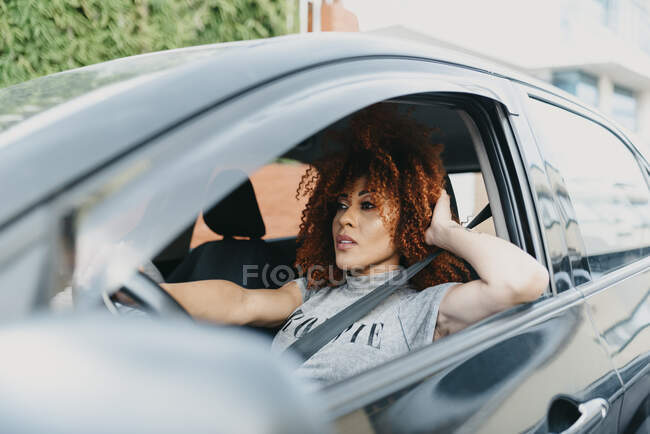 Jeune femme avec la main dans les cheveux voiture de conduite vu à travers la fenêtre — Photo de stock