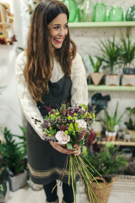 Улыбающаяся женщина, держащая букет цветов, стоя в цветочном магазине — стоковое фото