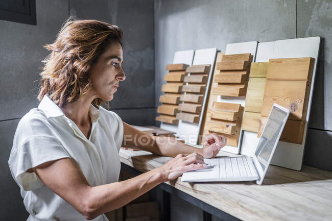 Mujer trabajando en el ordenador portátil con baldosas de madera en el escritorio en la oficina - foto de stock