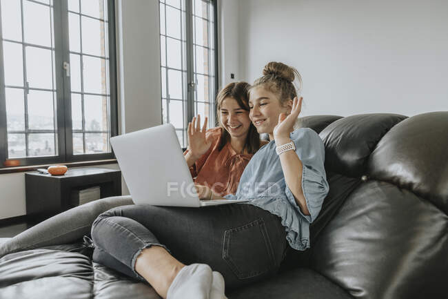 Amici che salutano mentre videoconferenza sul computer portatile sul divano di casa — Foto stock