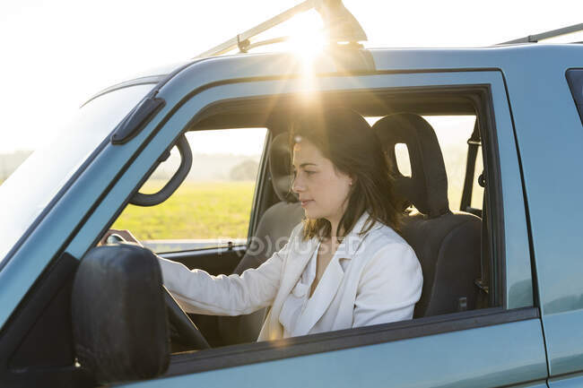 Beautiful woman on road trip driving car during sunset — Stock Photo