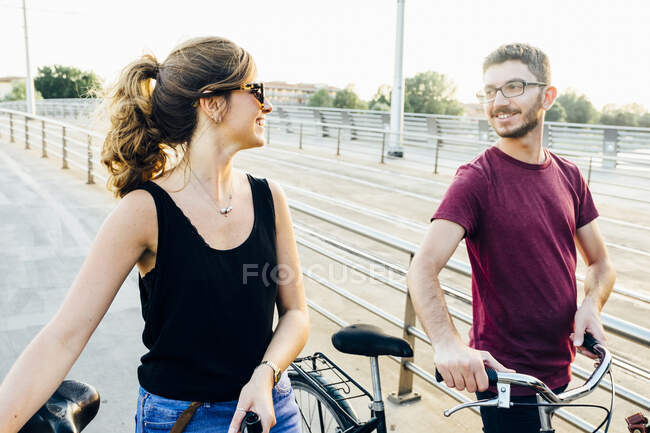 Couple parler tout en marchant avec des vélos sur le pont contre le ciel clair — Photo de stock