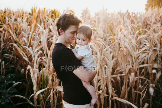 Padre portando bambino ragazzo mentre in piedi contro il campo durante il tramonto — Foto stock