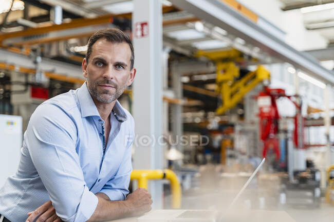 Fiducioso imprenditore di sesso maschile appoggiato alla scrivania in fabbrica — Foto stock