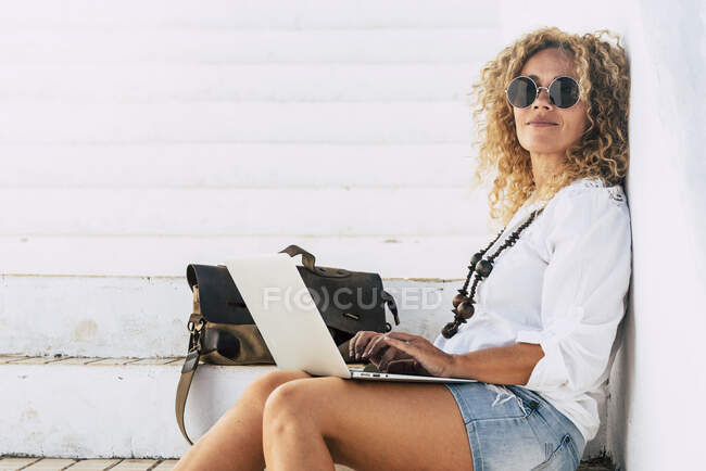 Femme confiante portant des lunettes de soleil à l'aide d'un ordinateur portable assis sur les marches — Photo de stock
