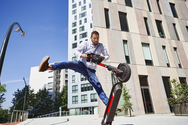 Entrepreneur jumping while holding motor scooter in city during sunny day — Foto stock