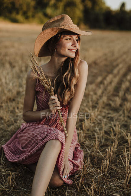 Happy woman sitting while looking away in wheat field during sunset — Stock Photo