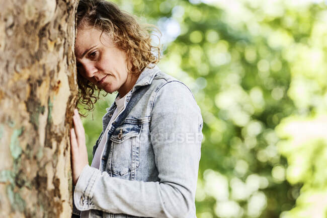 Primo piano di una donna premurosa appoggiata al tronco d'albero nel parco — Foto stock