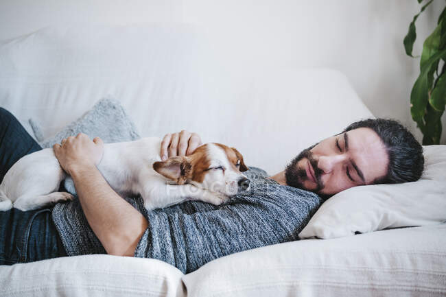 Uomo pisolino con cane mentre sdraiato sul divano a casa — Foto stock