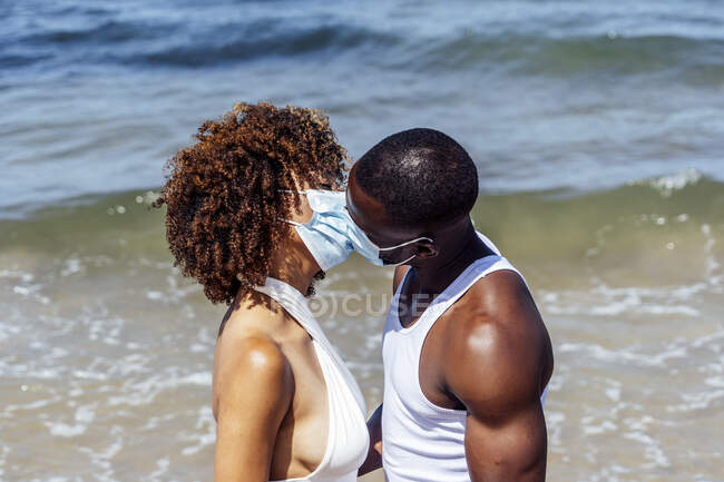 Paar mit Masken küsst sich, während es gegen das Meer steht — Stockfoto