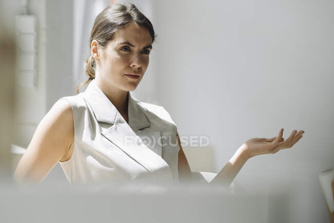 Young woman gesturing while sitting on chair at office — Stock Photo