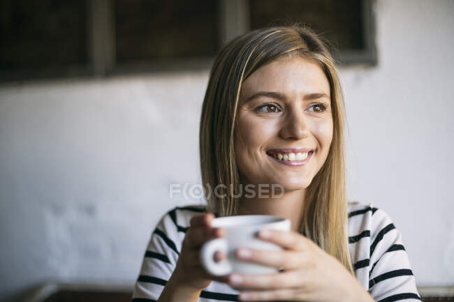 Donna sorridente guardando lontano mentre beve caffè nel caffè — Foto stock