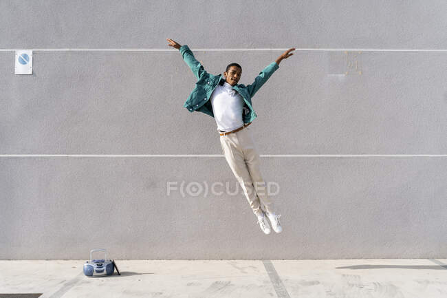 Junger Mann springt mit Radio auf Fußweg gegen graue Wand — Stockfoto