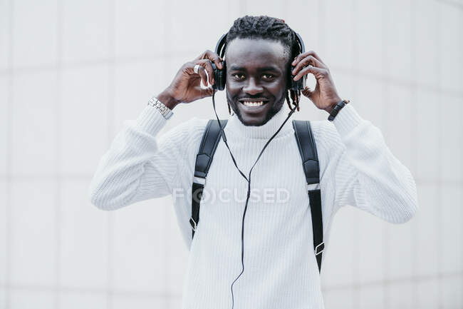 Hombre feliz usando auriculares mientras está de pie contra la pared blanca - foto de stock