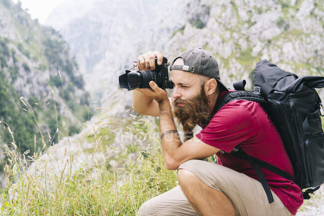 Young man taking photo through camera while sitting on mountain at Ruta Del Cares, Asturias, Spain — Stock Photo