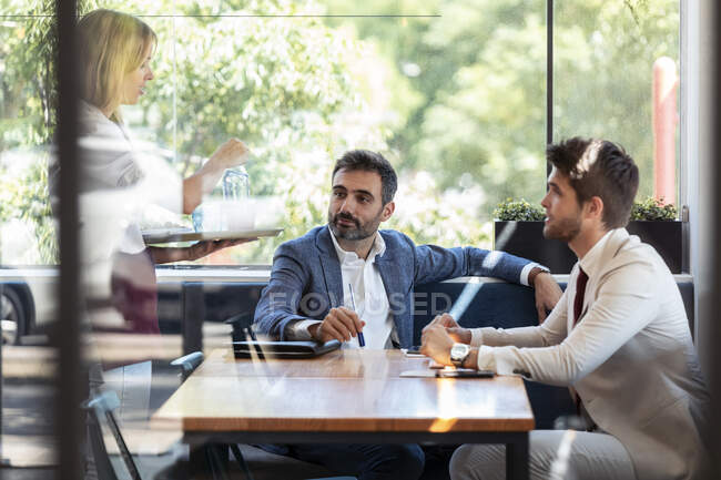 Empresarios sentados a la mesa dando orden a camarera en restaurante - foto de stock