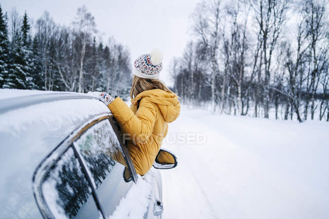Woman looking at bare trees while leaning out through car window during winter — Stock Photo