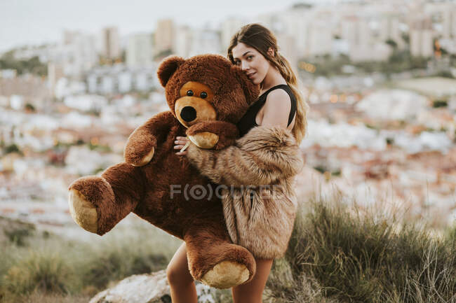 Молодая женщина обнимает плюшевого медведя в то время как город в фоновом режиме — стоковое фото