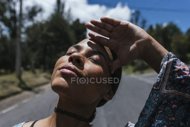 Primer plano de la mujer joven con los ojos cerrados de pie en la carretera durante el día soleado - foto de stock