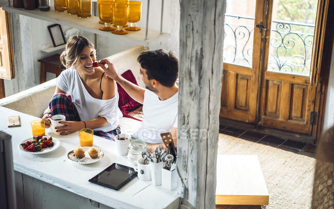 Молодий чоловік годує дівчину полуницею під час сніданку вдома — стокове фото