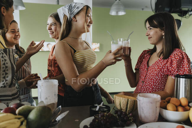 Ragazze adolescenti in piedi in cucina degustazione con frullati di frutta fresca — Foto stock