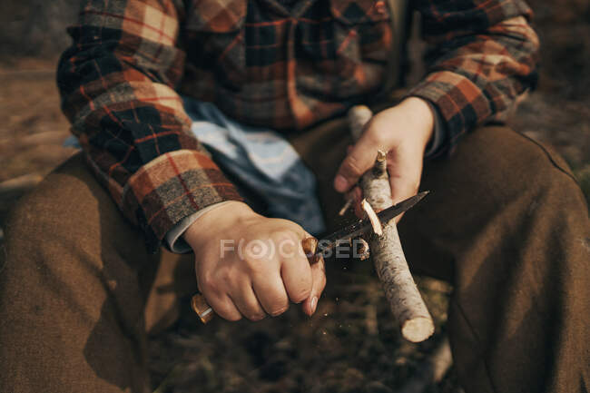 Bushcrafter palo de corte mientras está sentado en el bosque - foto de stock