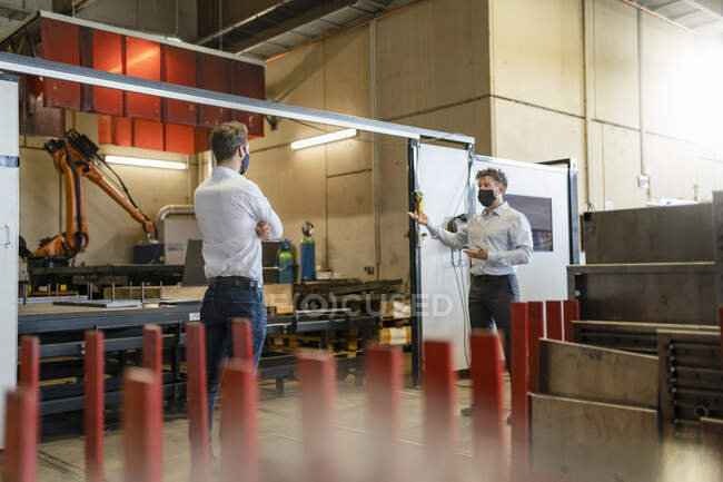 Бізнесмени, одягнені в маску, стоять на соціальній відстані під час роботи на заводі. — стокове фото