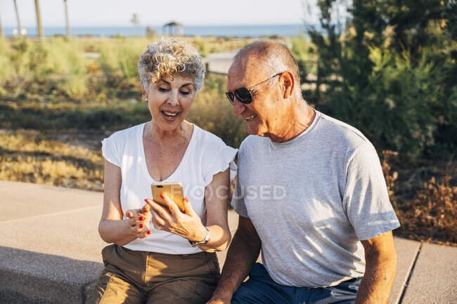 Senior man and woman using phone while sitting at park — Stock Photo