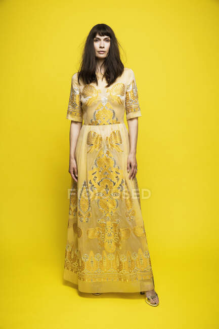 Mujer madura vistiendo vestido de pie sobre fondo amarillo - foto de stock