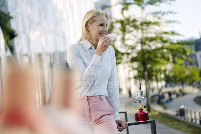 Щаслива жінка-підприємець, дивлячись далеко, тримаючи чашку кави у фінансовому районі — стокове фото