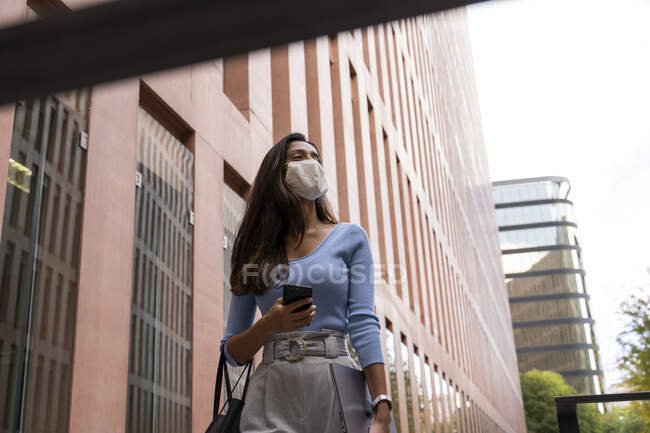 Безробітна жінка в масці обличчя, яка відводить погляд під час прогулянки по офісному будинку під час COVID-19 — стокове фото