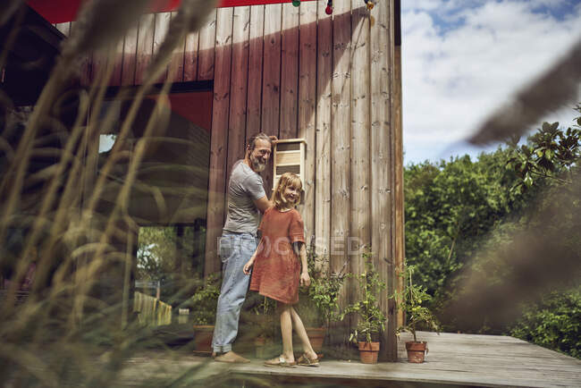 Sonriente padre e hija mirando hacia otro lado mientras instalan insecto hotel en la pared - foto de stock