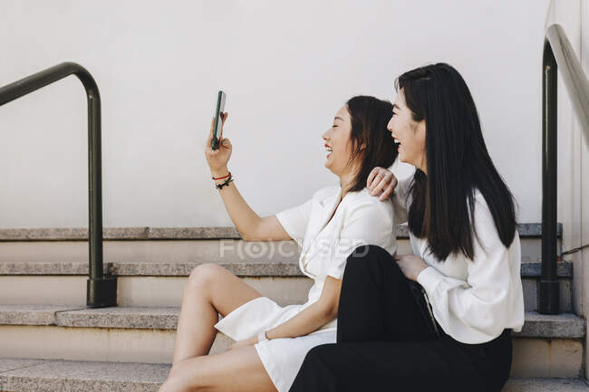 Compañeros de trabajo tomando selfie mientras están sentados en la escalera - foto de stock