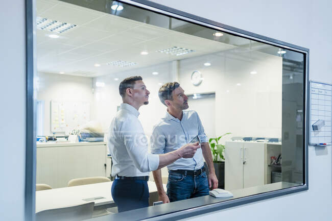 Uomo d'affari con collega maschio che guarda attraverso la finestra di vetro mentre lavora in fabbrica — Foto stock