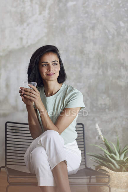 Donna d'affari che tiene frullato contemplare mentre seduto sulla sedia contro il muro in ufficio — Foto stock