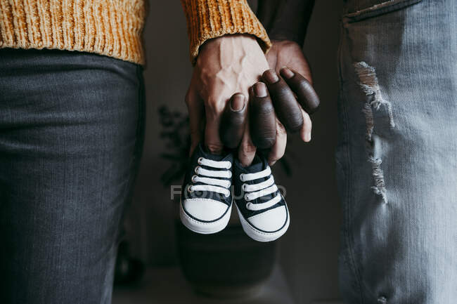 Jeune homme avec une femme enceinte tenant des chaussons de bébé à la maison — Photo de stock