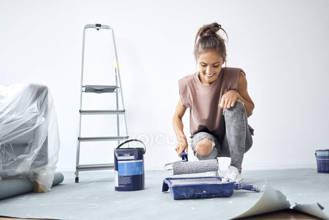 Smiling woman holding paint roller while crouching at home — Stock Photo