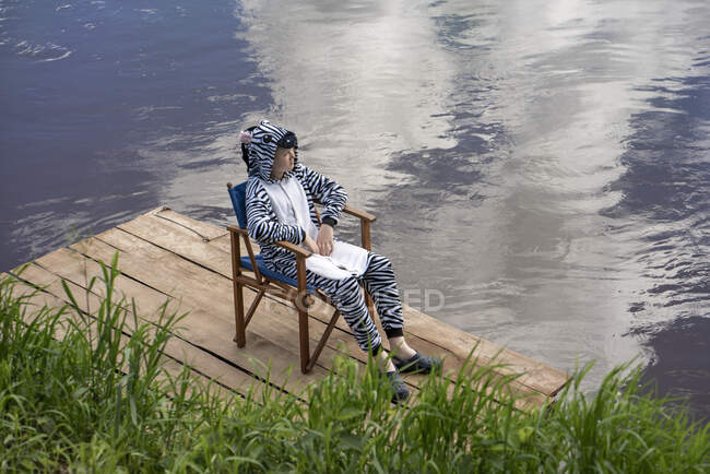 Boy wearing zebra costume sitting by lake — Foto stock